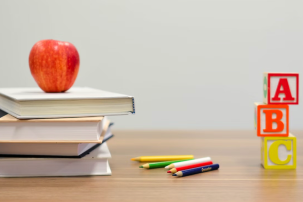 An image of books, an apple, pencils and number blocks on a table