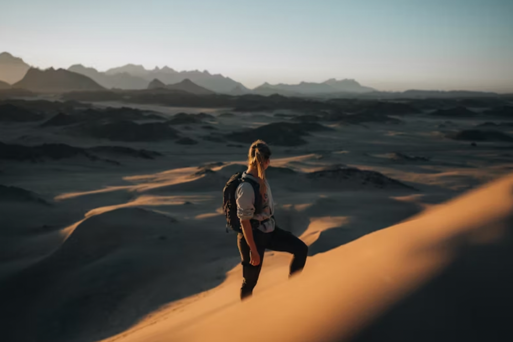 An image of a woman climbing sand dunes in a desert