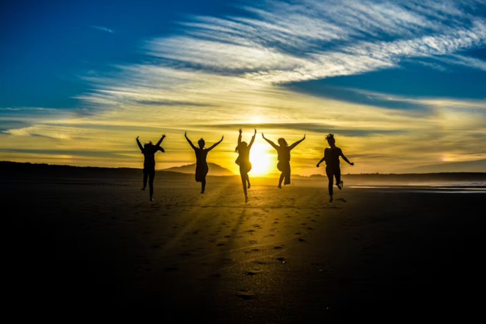 An image of people jumping on a beach in front of a sunset