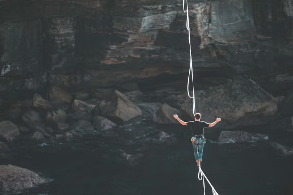 An image of a man walking across a tightrope over mountains